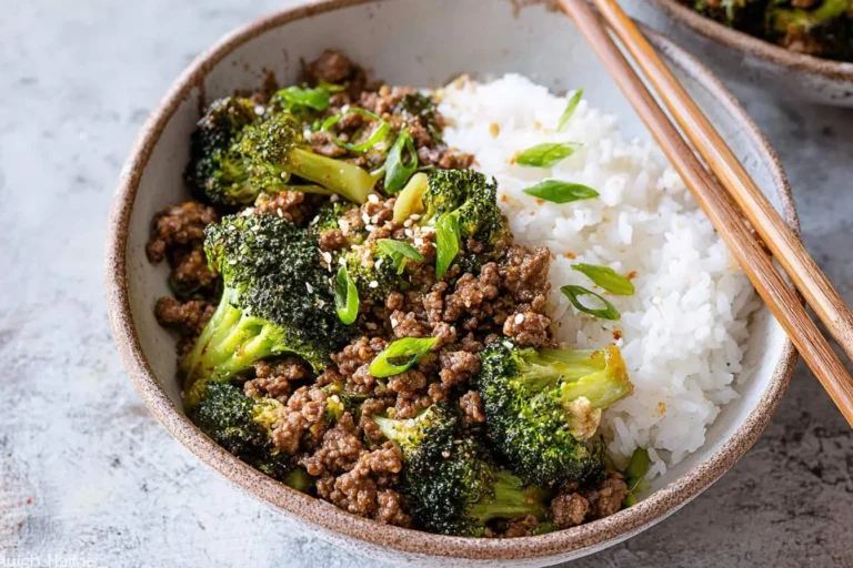 A rustic bowl of savory ground beef and broccoli stir-fry served alongside fluffy white rice, garnished with sesame seeds and green onions.