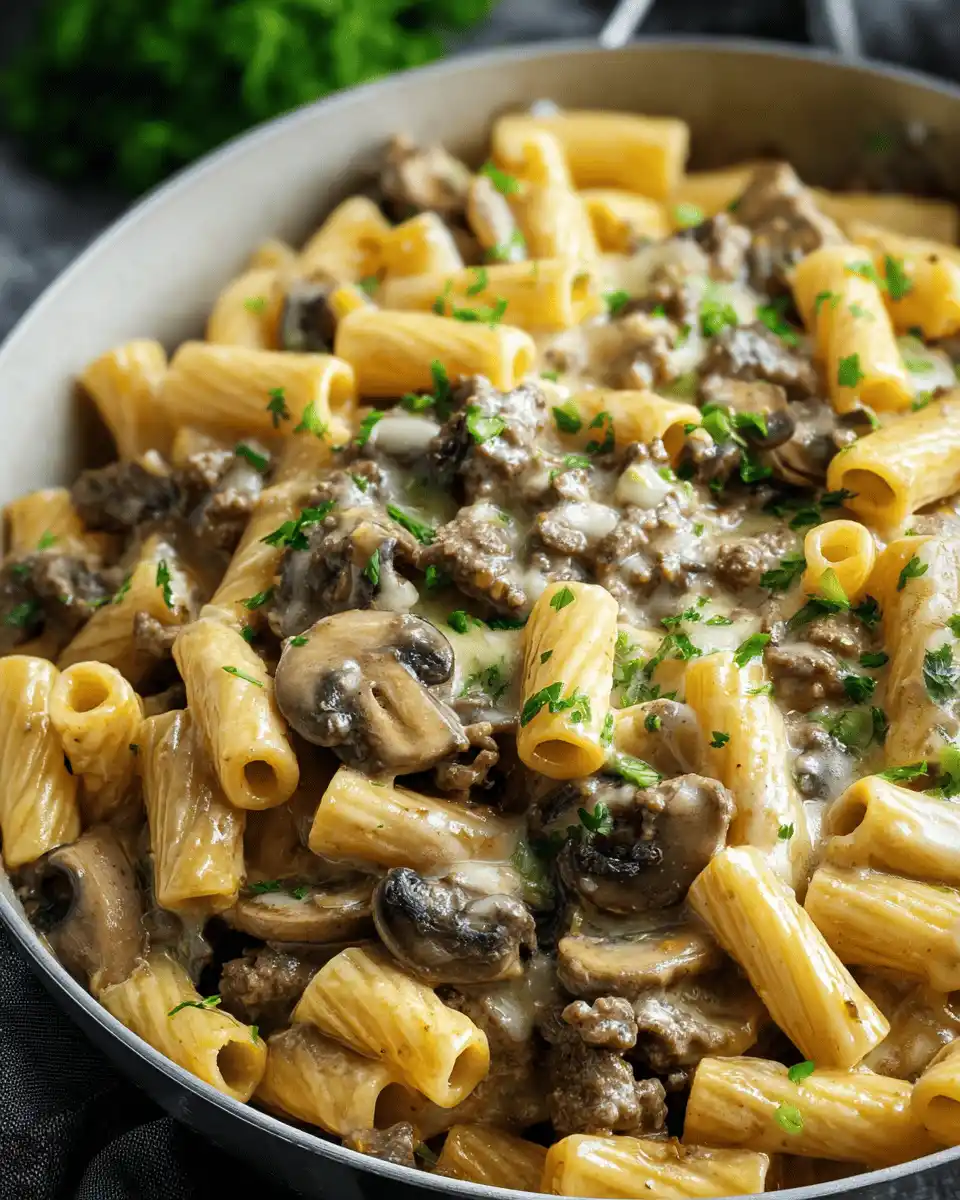Close-up of Philly cheesesteak pasta with rigatoni, ground beef, mushrooms, and melted cheese, garnished with fresh parsley in a skillet.
