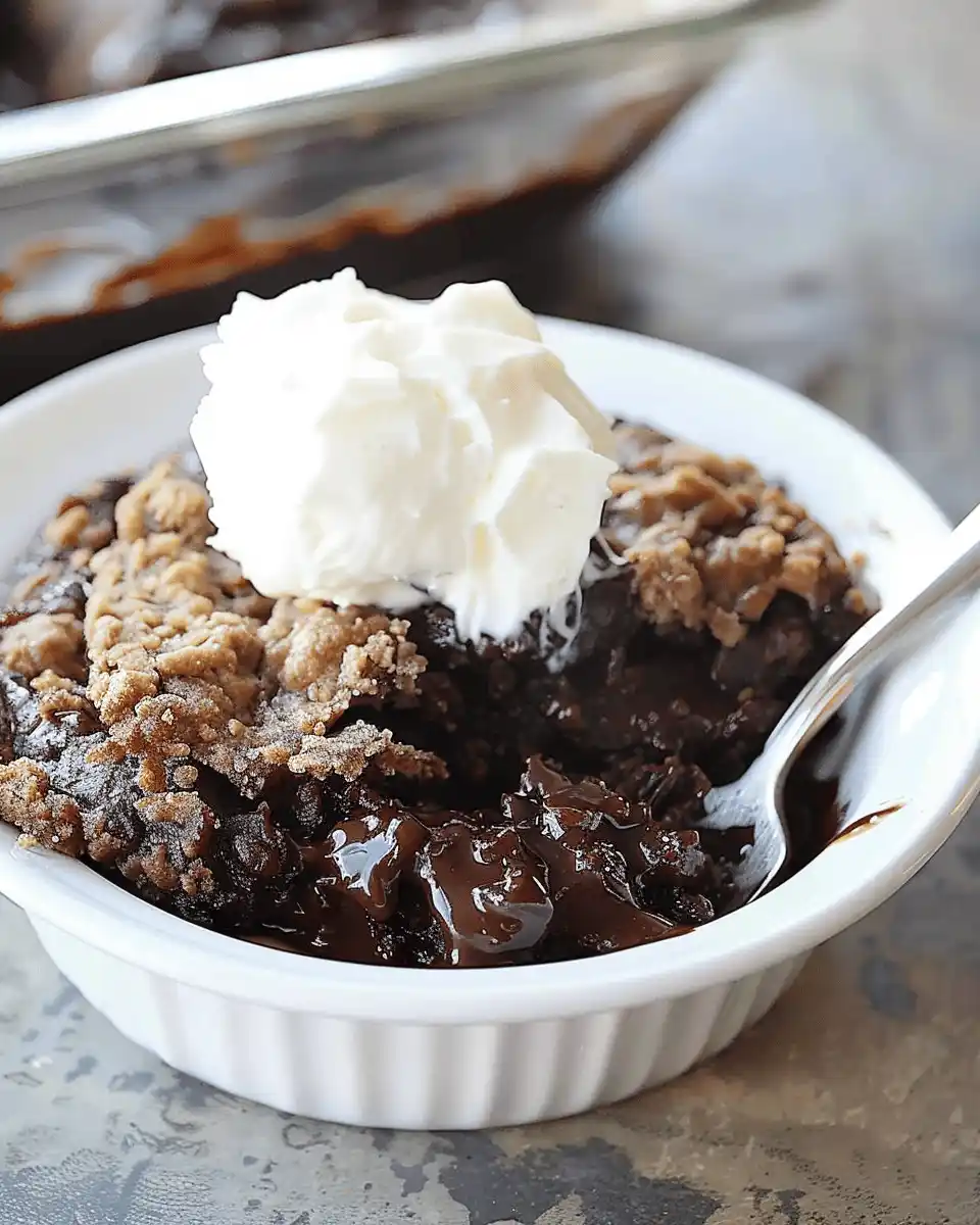 Warm southern chocolate cobbler with a brownie-like topping, gooey chocolate pudding center, and whipped cream on top.