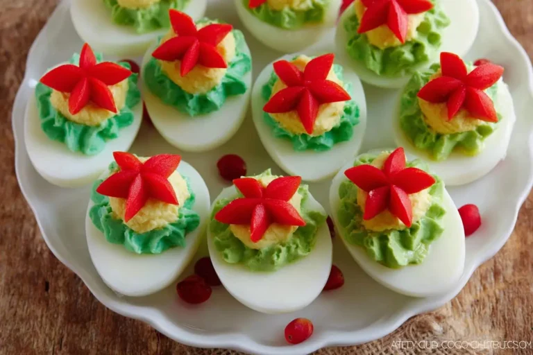 A white plate filled with festive christmas deviled eggs, each topped with green piped avocado or pesto and a red bell pepper star.
