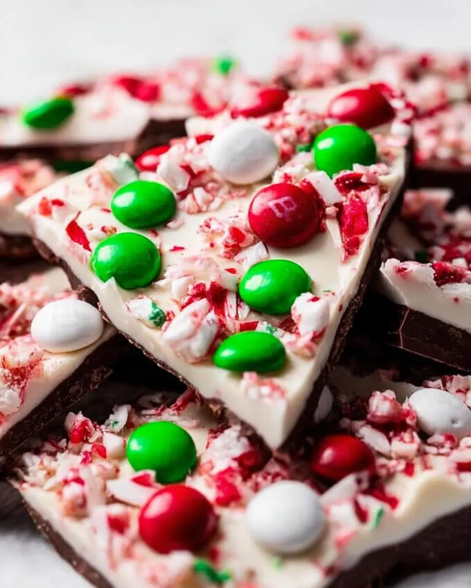 Close-up of festive homemade peppermint bark pieces layered with dark and white chocolate, crushed candy canes, and colorful M&M candies.