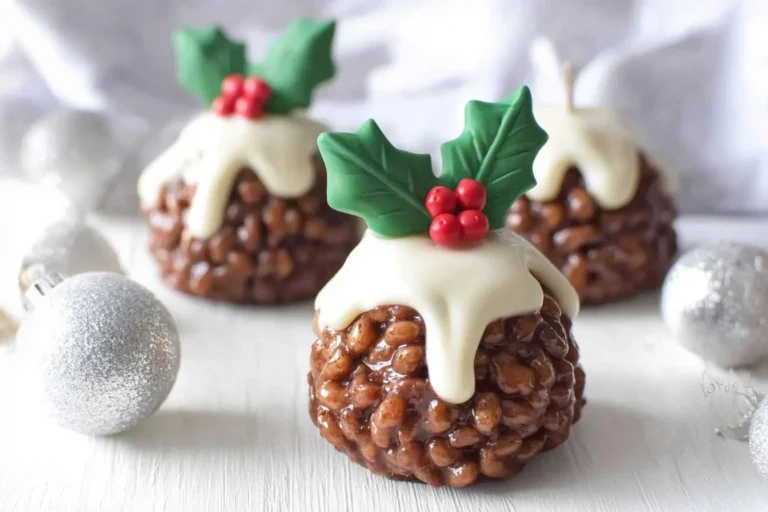 Three festive Rice Krispie Christmas Puddings topped with white icing, green holly, and red berries, surrounded by silver baubles.