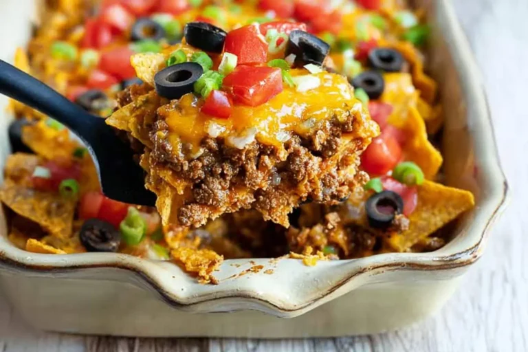 A serving of cheesy Taco Casserole with seasoned ground beef, melted cheese, diced tomatoes, sliced black olives, and green onions being lifted from a baking dish.