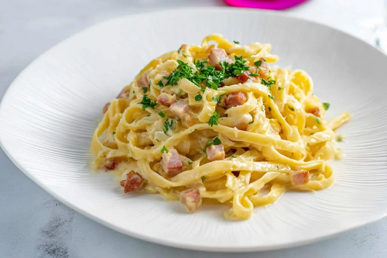 A close-up shot of a plate of creamy pasta Carbonara, garnished with fresh chopped parsley and crispy bacon bits.
