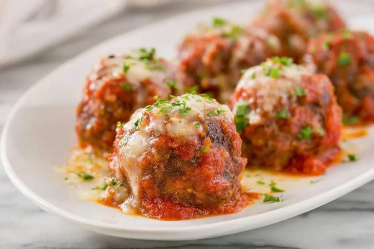 A close-up shot of several Cheesy Mozzarella Meatballs covered in rich red sauce and fresh parsley on a white plate.