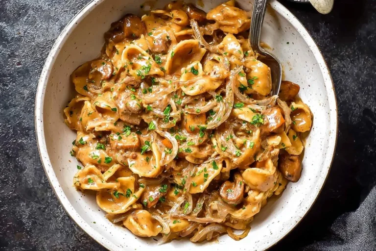 Overhead shot of a bowl of creamy French Onion Pasta with caramelized onions, beef, and fresh parsley, with a fork.