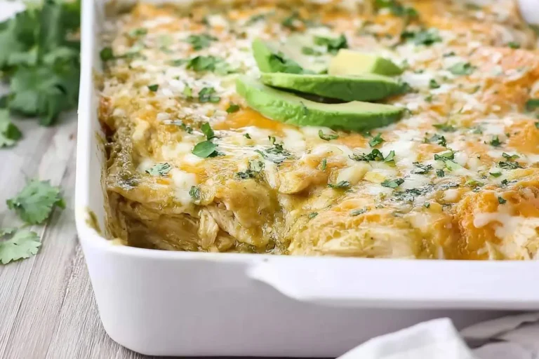 A close-up of a bubbling green chicken enchilada casserole in a white baking dish, garnished with melted cheese, fresh cilantro, and avocado slices.
