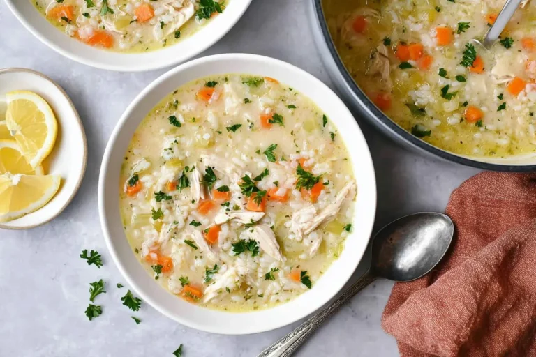 Two bowls and a pot of creamy lemon chicken rice soup, garnished with parsley and served with fresh lemon wedges on the side.