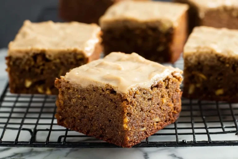 A close-up of moist banana bread brownies with a thick layer of brown sugar frosting on a black wire cooling rack.