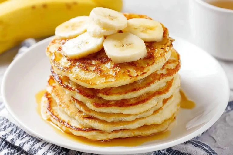 A delicious stack of golden banana pancakes drizzled with syrup and topped with fresh banana slices on a white plate.