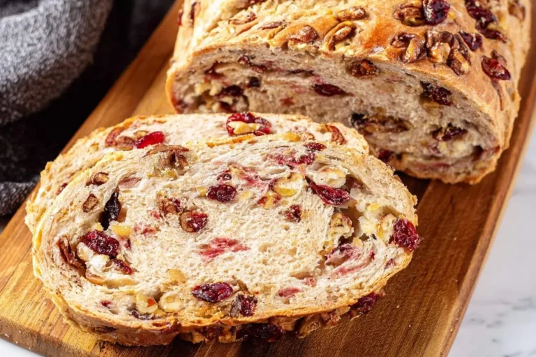 A close-up view of a loaf of Cranberry Walnut Bread, with several slices cut and displayed on a wooden board.