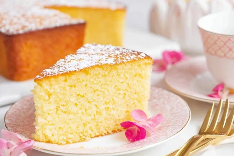 A golden slice of French Butter Cake, generously dusted with powdered sugar, resting on a pink patterned plate.