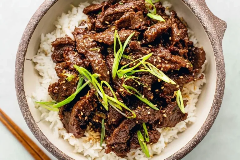 A close-up of a rustic bowl filled with fluffy white rice topped with savory Korean Beef Bulgogi, garnished with fresh green onions and sesame seeds.