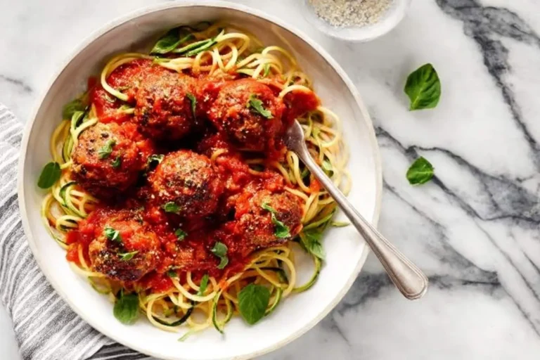 A white bowl of homemade Meatballs and Spaghetti with zucchini noodles, garnished with fresh basil and parmesan cheese.