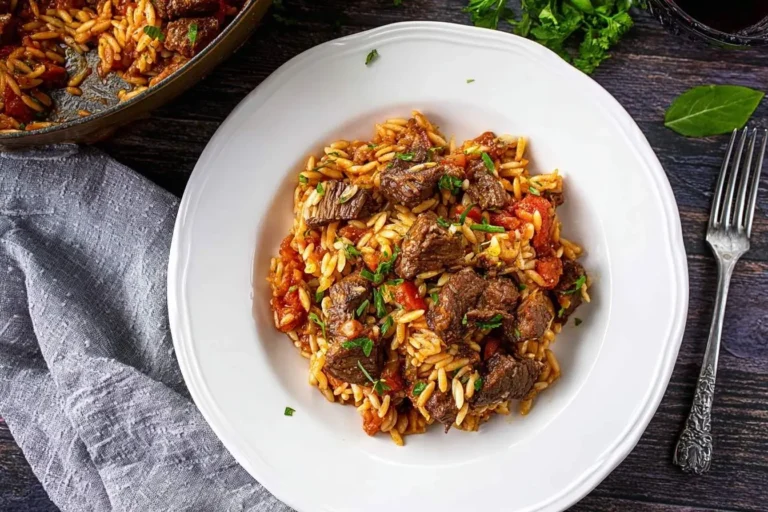 A plate of hearty One Pot Beef Giouvetsi with tender beef, orzo pasta, and a rich tomato sauce, garnished with fresh herbs.