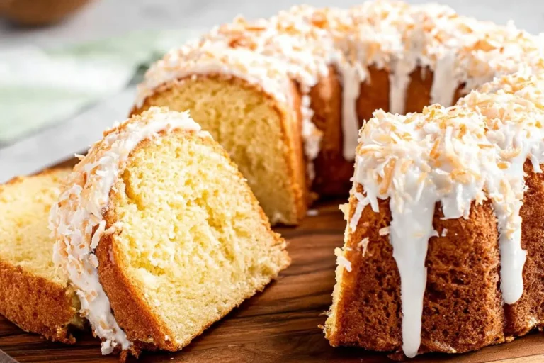 A golden pina colada pound cake, sliced and topped with white icing and toasted coconut flakes, presented on a wooden board.