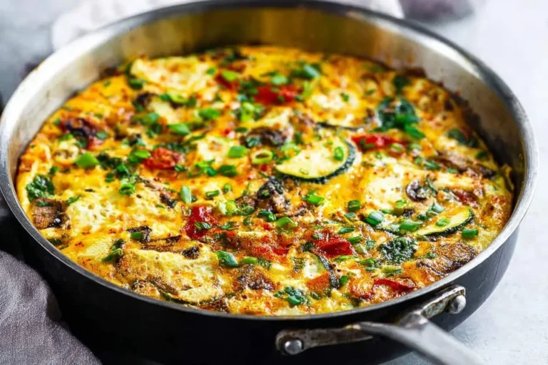 A colorful veggie frittata cooked in a skillet, brimming with zucchini slices, diced tomatoes, and green chives.