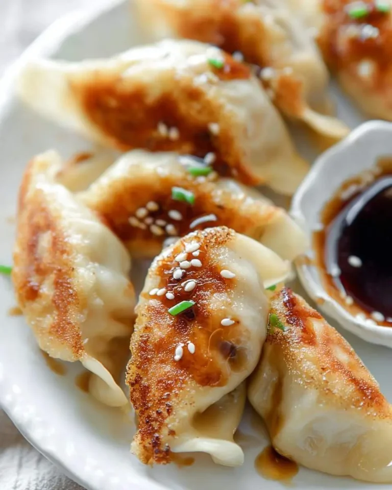 Close-up of golden-brown pan-fried Chicken Potstickers, topped with sesame seeds and chives, served with a rich dipping sauce.