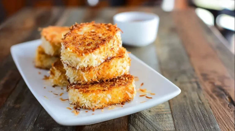 A stack of golden brown coconut-crusted French toast slices on a white rectangular plate, set on a rustic wooden table.