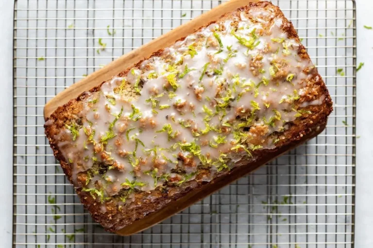 Overhead shot of a freshly baked loaf of Coconut Lime Glazed Banana Bread, topped with a shiny white glaze and vibrant lime zest, resting on a cooling rack.