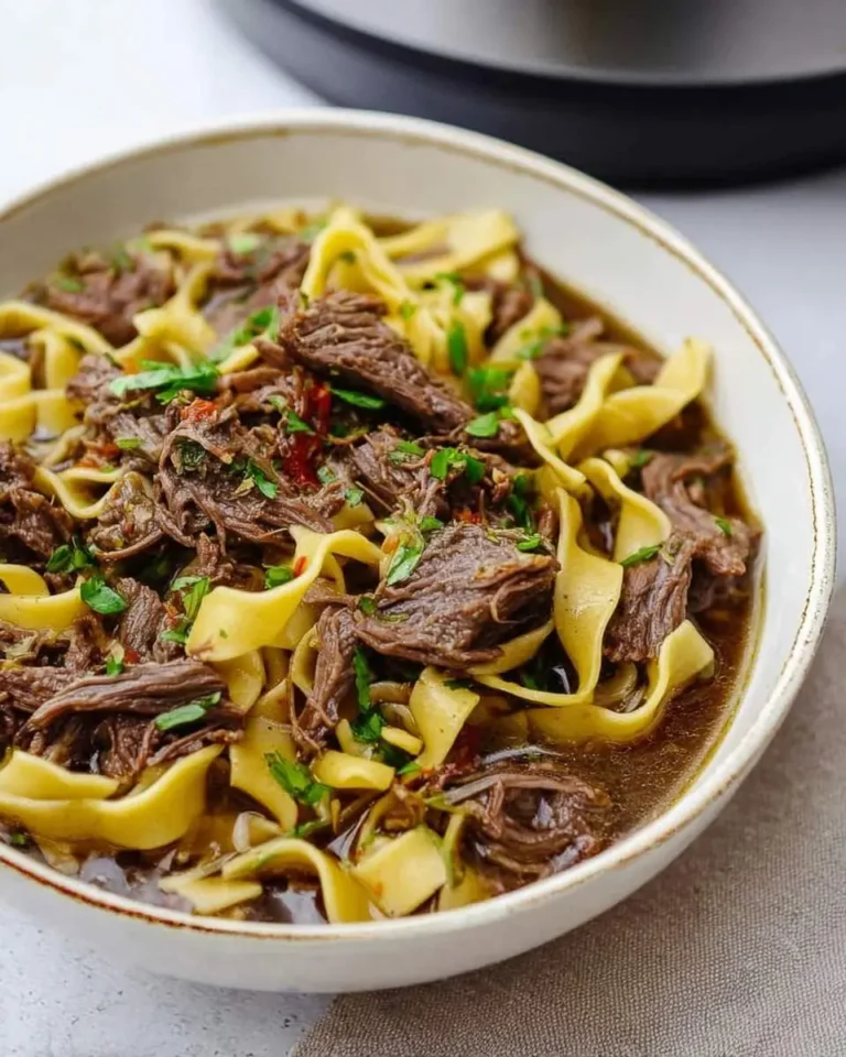 A close-up view of a bowl of hearty Crock Pot Mississippi Beef Noodles, garnished with fresh chopped herbs.