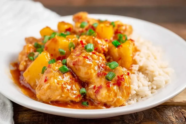 A close-up of Crockpot Hawaiian Chicken with pineapple, green onions, and chili flakes, served with white rice on a white plate.
