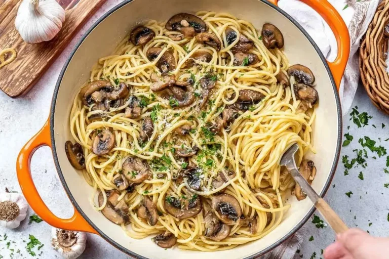 A top-down view of a vibrant orange pot filled with freshly cooked Mushroom and Garlic Spaghetti, garnished with parsley and cheese.