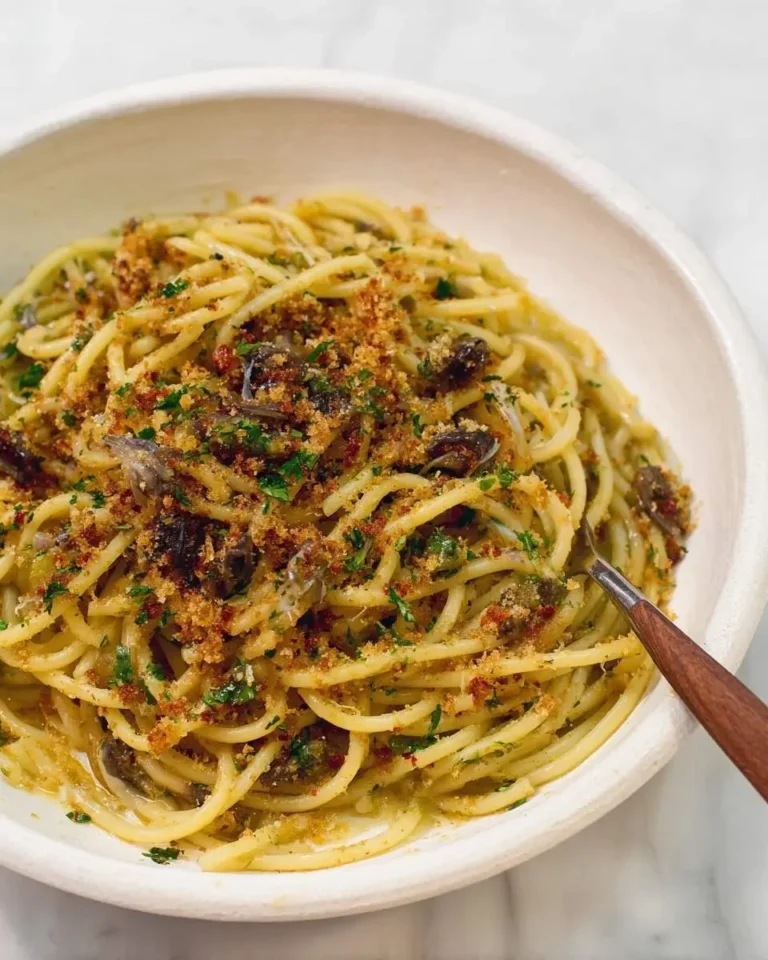 Close-up of a white bowl filled with Anchovy Pasta with Breadcrumbs and fresh parsley, with a fork resting in it.