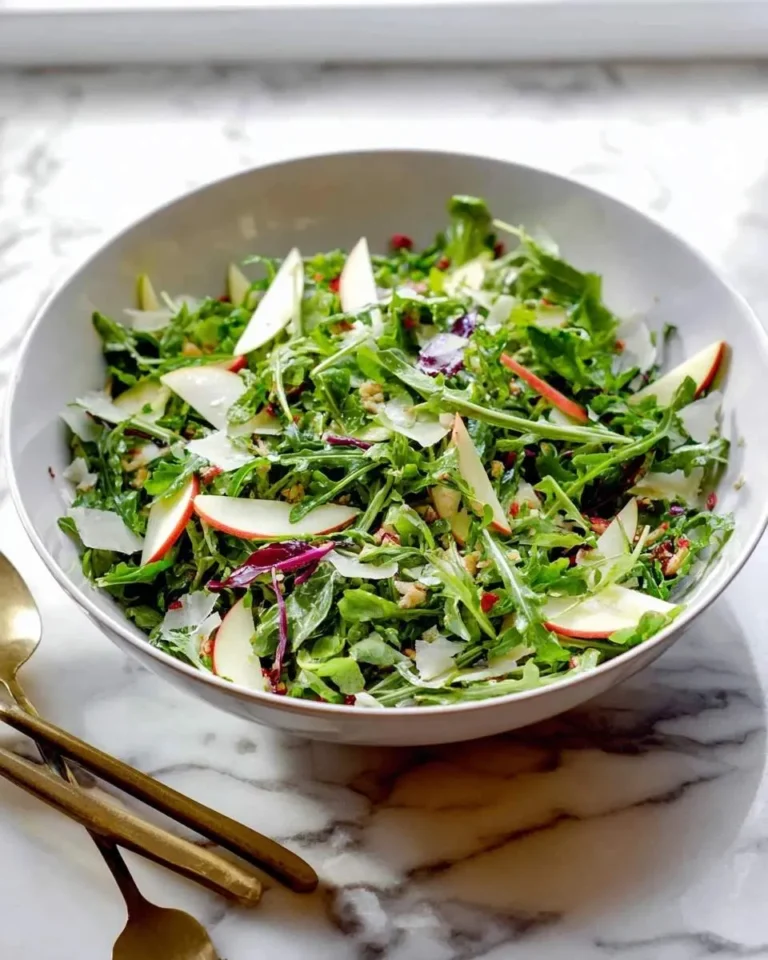 A vibrant Apple Arugula Salad with crisp greens, thinly sliced apples, shaved Parmesan, walnuts, and pomegranate seeds.
