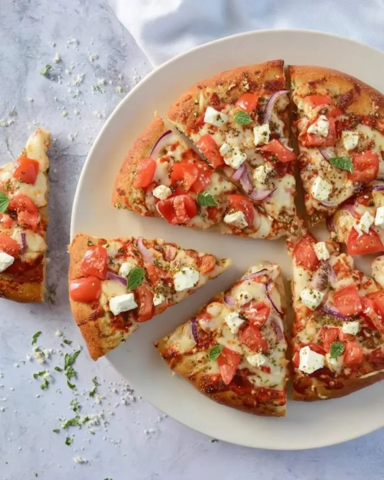 A vibrant Bruschetta Pizza, topped with fresh tomatoes, feta, red onion, and herbs, sliced on a plate with one piece separate.