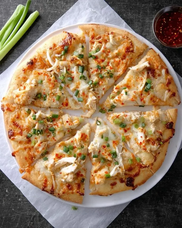 A delicious Crab Rangoon Pizza, cut into slices, topped with white meat, melted cheese, and fresh green onions, on a white plate.