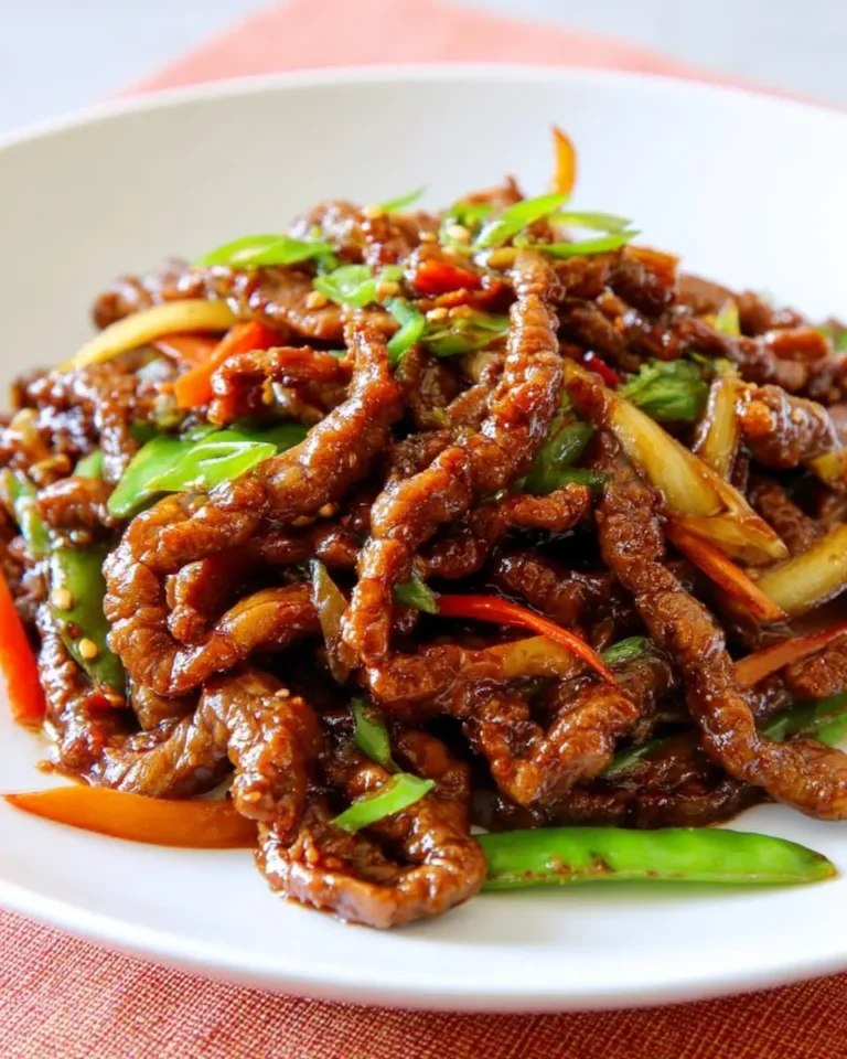Close-up of a white plate filled with delicious crispy Ginger Beef stir-fry, featuring glossy beef strips, green beans, and red peppers.