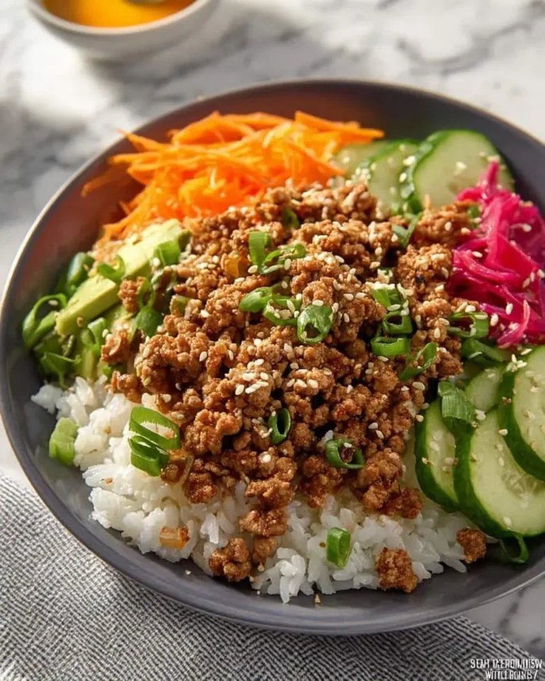 A colorful ground turkey bowl with white rice, sesame-crusted ground turkey, shredded carrots, sliced cucumbers, avocado, and pickled red cabbage, garnished with green onions.