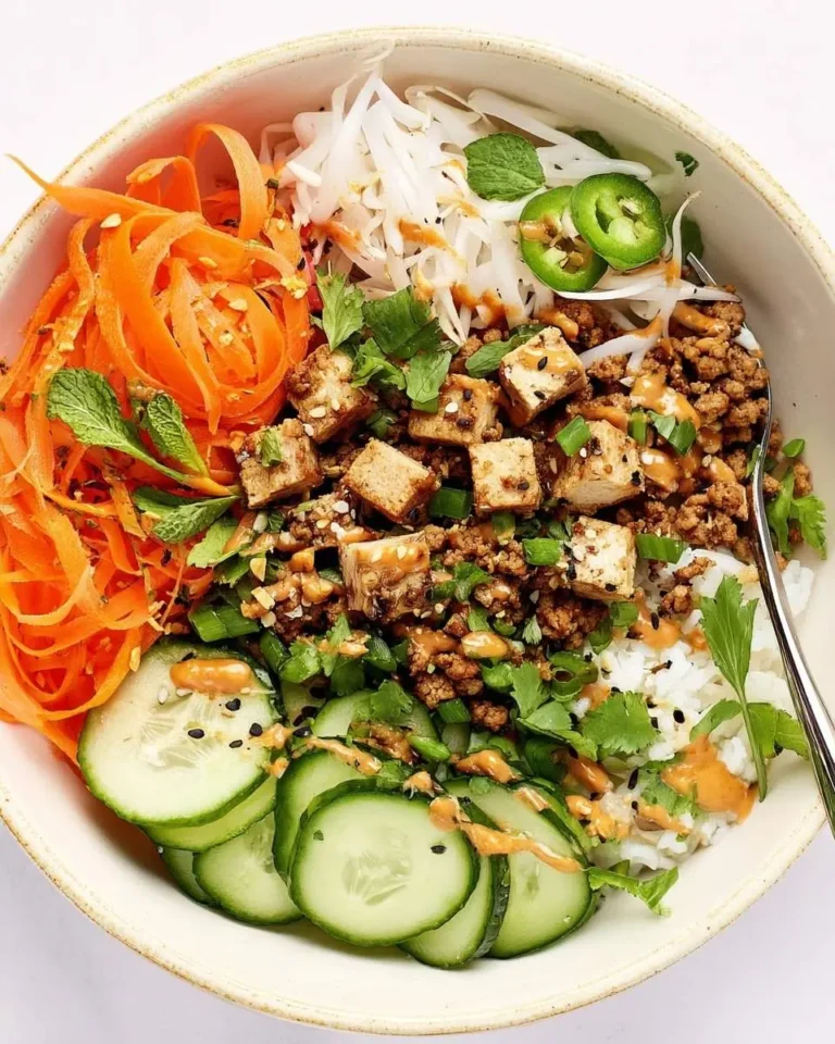 A vibrant Healthy Banh Mi Bowl featuring crisp carrot ribbons, sliced cucumbers, white radishes, savory protein, tofu, and a creamy sauce drizzle.