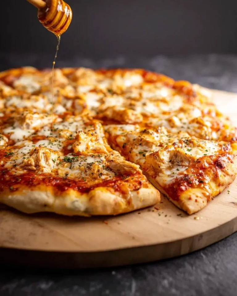 A close-up of a delicious hot honey pizza with chicken and melted cheese, being drizzled with honey from a dipper.