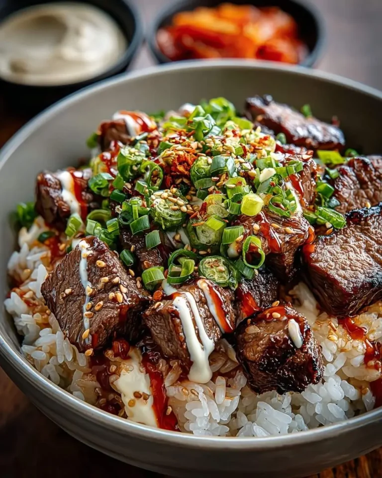 A close-up of a delicious Korean BBQ Steak Rice Bowls dish, featuring grilled steak cubes, white rice, green onions, sesame seeds, and various sauces.