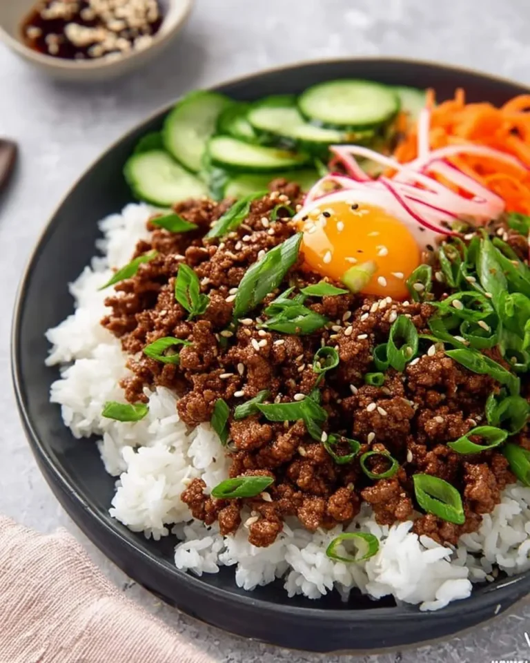 A delicious Korean Ground Beef Bowl with seasoned ground beef, white rice, a raw egg yolk, green onions, sesame seeds, sliced cucumbers, shredded carrots, and radishes.