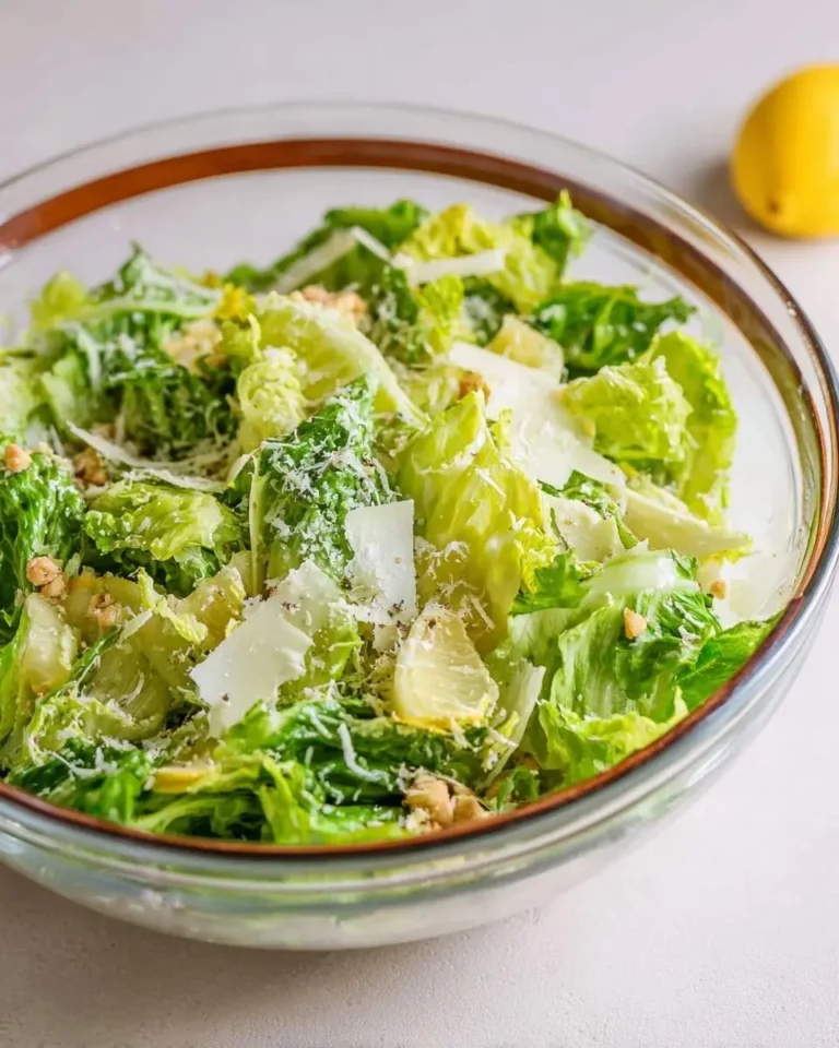 A clear glass bowl filled with a fresh Lemon Parmesan Lettuce Salad, featuring crisp greens, shaved cheese, and a whole lemon nearby.