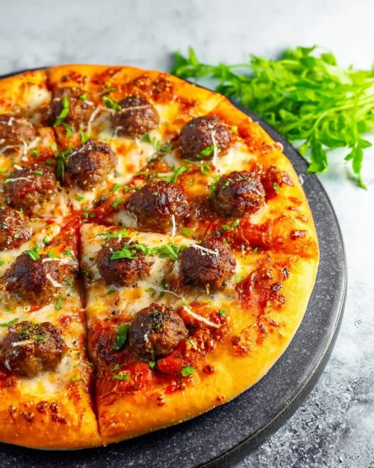 A delicious, freshly baked meatball pizza with melted cheese, savory meatballs, and fresh herbs, served on a dark stone board.