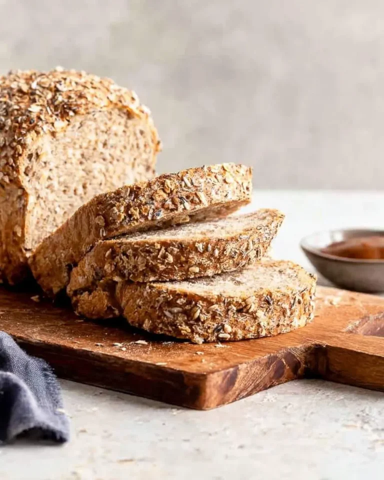 Slices of freshly baked multigrain bread on a rustic wooden cutting board, with the remaining loaf in the background.