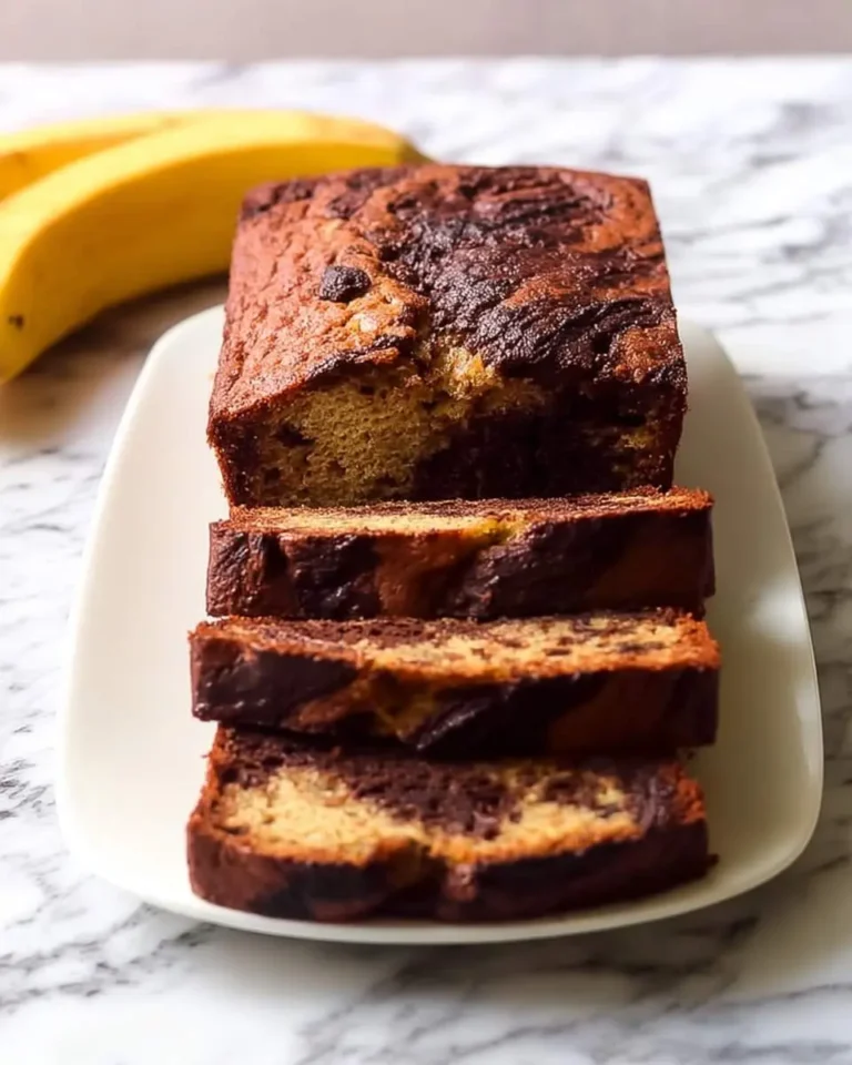 A delicious loaf of Nutella Banana Bread, partially sliced to reveal its marbled interior, with fresh bananas in the background.