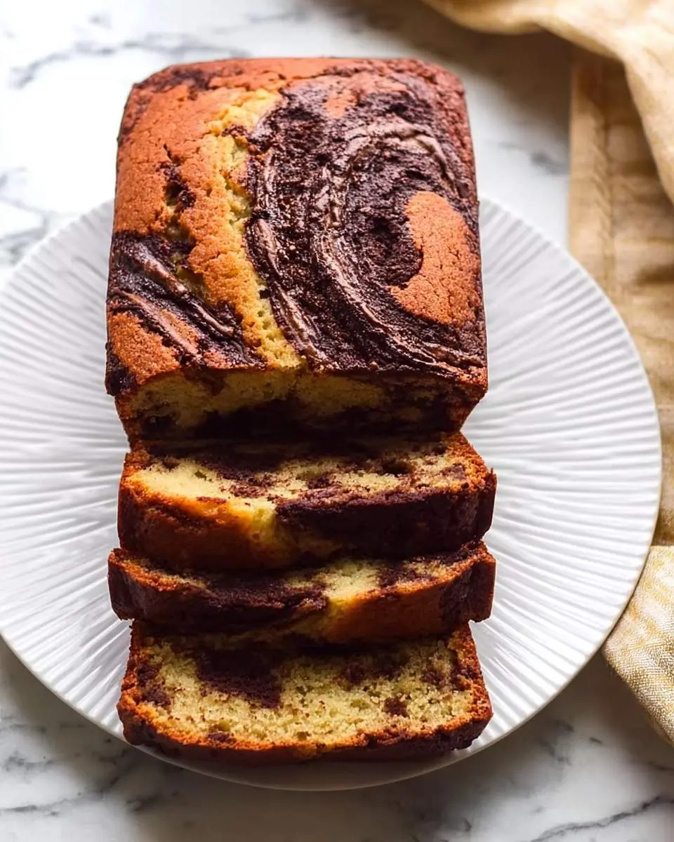 A sliced loaf of marbled Nutella Banana Bread on a white plate, showcasing its beautiful brown and beige swirled pattern.
