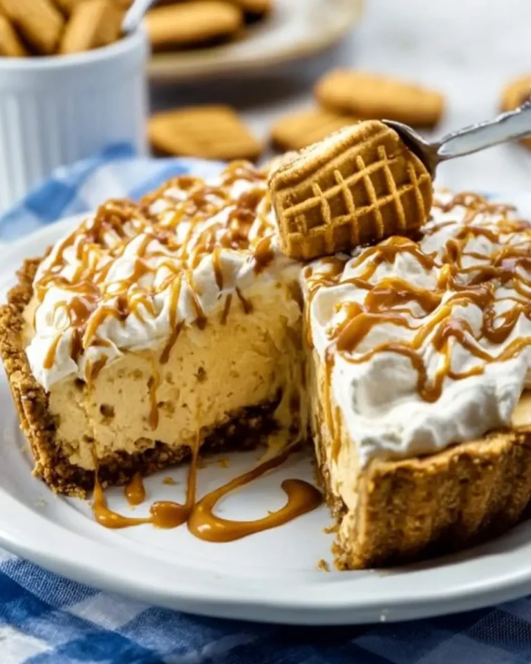 A slice of Nutter Butter Pie with creamy filling, crumb crust, whipped cream, and caramel drizzle, with a Nutter Butter cookie on a spoon.