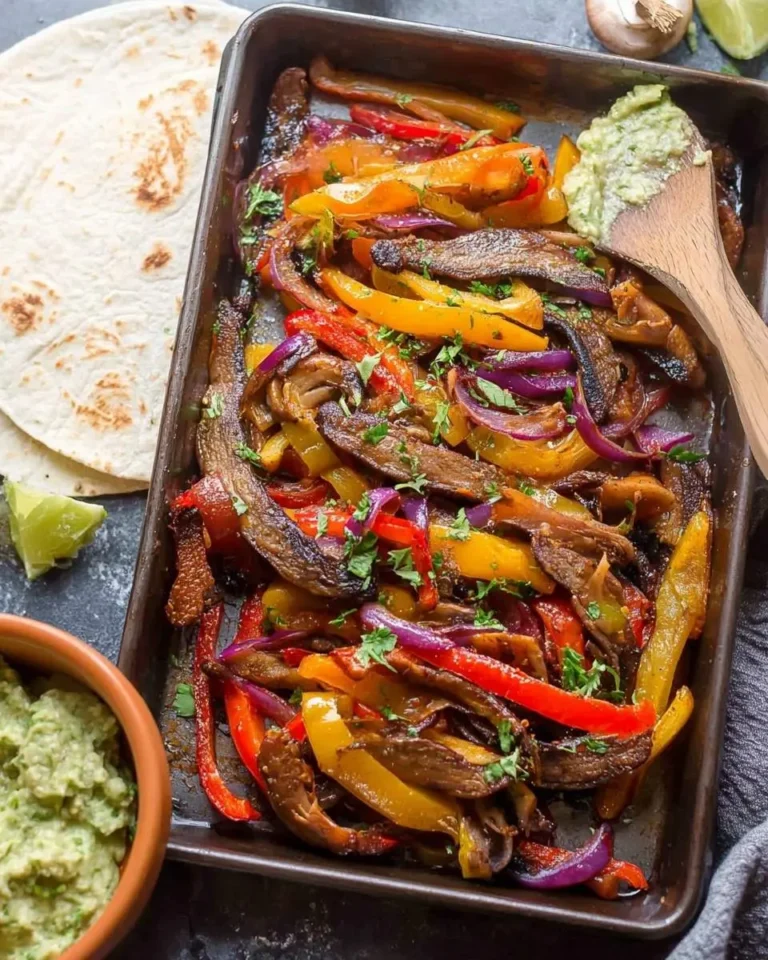 A baking sheet filled with vibrant Portobello Mushroom Fajitas, featuring sliced bell peppers, red onions, and mushrooms, garnished with herbs, served with tortillas and guacamole.