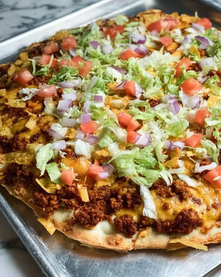 A vibrant, fully loaded Taco Pizza on a metal baking sheet, topped with seasoned beef, melted cheese, lettuce, tomatoes, and red onions.