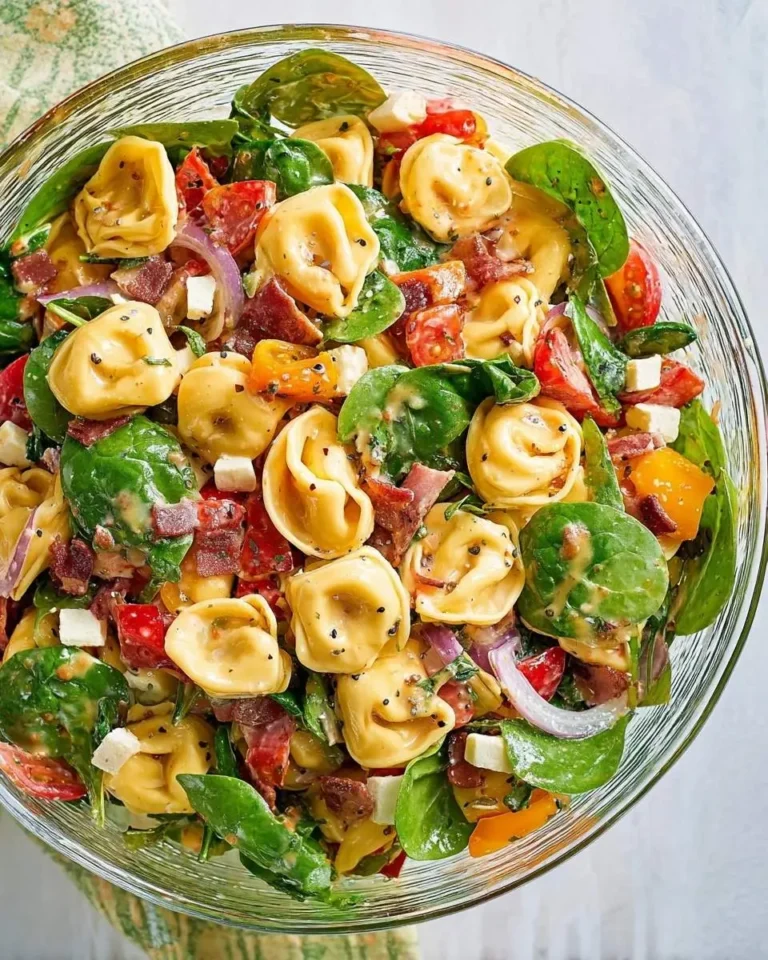 Vibrant Tortellini Pasta Salad in a glass bowl, featuring cheese tortellini, spinach, tomatoes, bacon, red onion, feta, and creamy dressing.