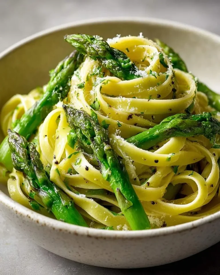 A close-up of a serving of fresh Asparagus Ribbon Pasta in a light bowl, garnished with grated cheese and fresh herbs.