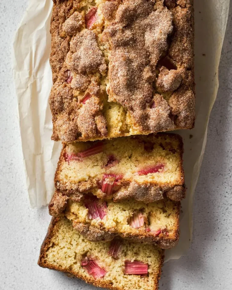 Overhead view of a delicious Buttermilk Rhubarb Bread loaf, partly sliced to show the pink rhubarb pieces and crumbly topping.