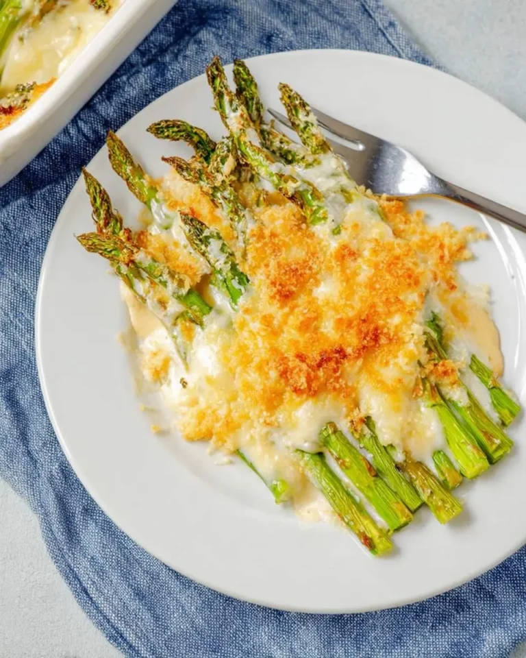 A delicious serving of Cheesy Asparagus casserole on a white plate, topped with melted cheese and golden breadcrumbs.