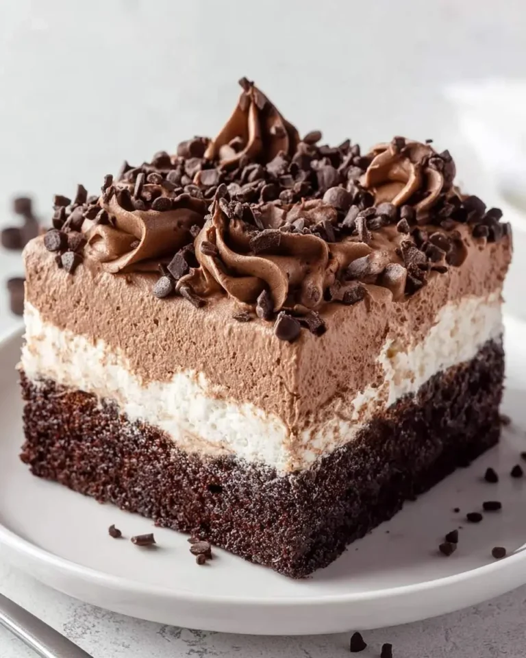 A mouth-watering slice of layered chocolate poke cake with dark cake, white cream, chocolate mousse, and chocolate chip topping.